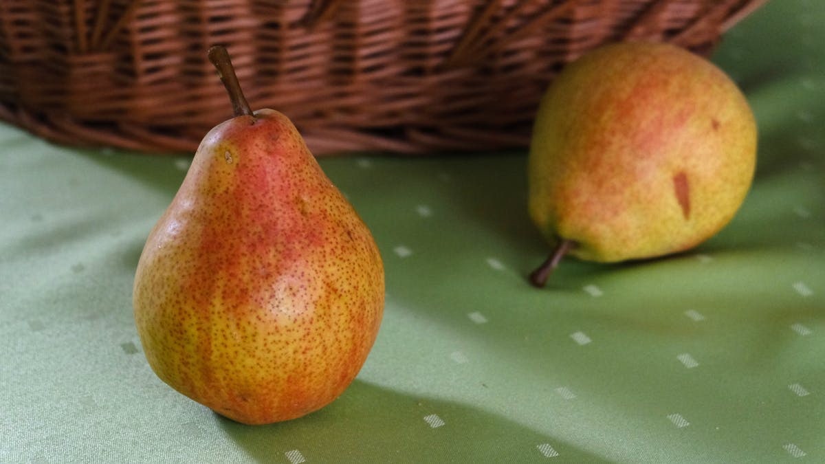 Two ripe pears on a green tablecloth beside a wicker basket, evoking rustic charm.